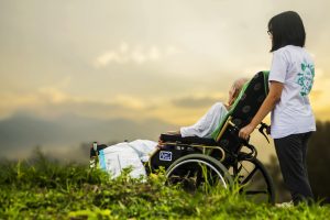 “hospice-1821429_960_720.jpg” by truthseeker08 is licensed under CC0 Image showing a caretaker assisting a hospice patient reclining in a wheelchair