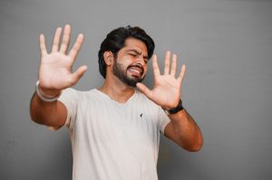 Image showing a man, facing camera, with pained expression and hands up in a defensive position